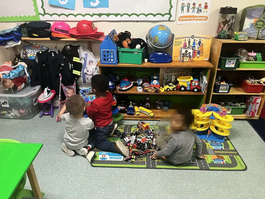 Children playing with toy cars in front of dress-up and toy shelves